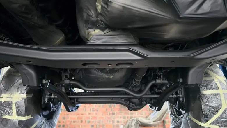 Masked up mid-treatment — body, tank and brake lines wrapped before anything is applied